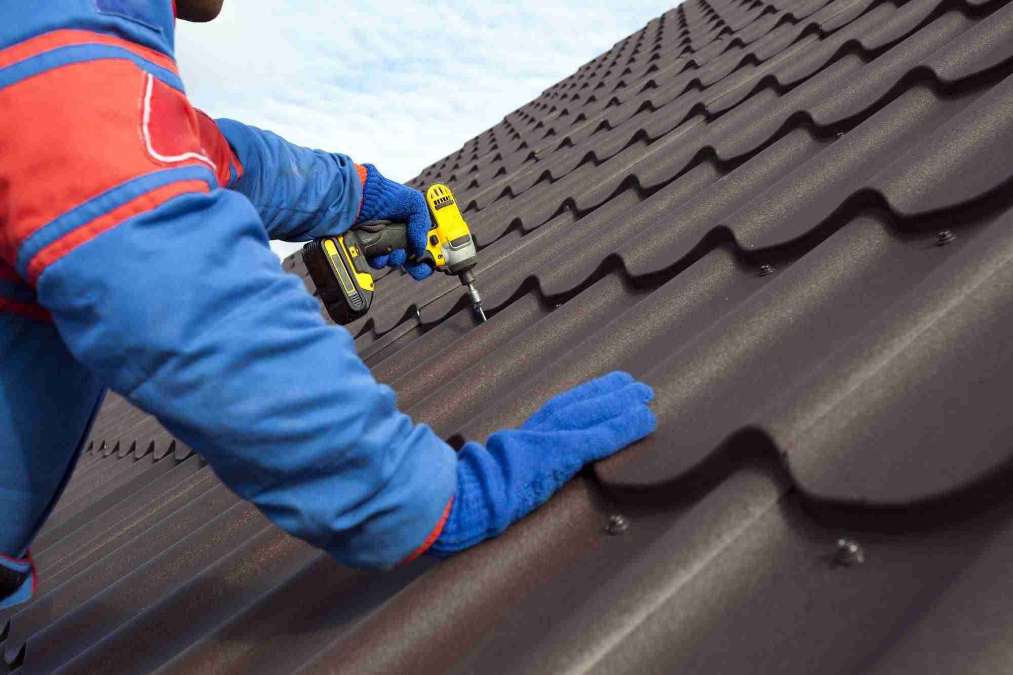 Man worker uses a power drill to attach a cap metal roofing job with screws.